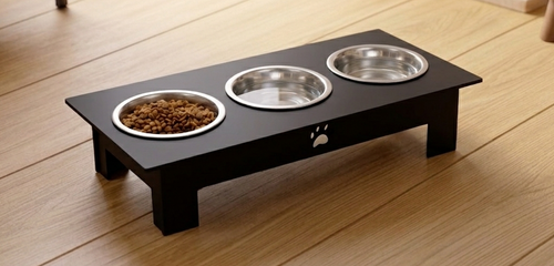 A black elevated pet feeder stand with three stainless steel bowls, shown on a light wood floor. One bowl contains dry dog food.