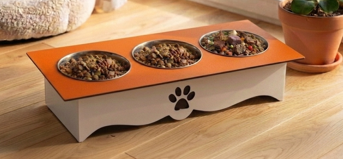 A three-compartment elevated pet feeder with a white base, orange top panel, and stainless steel bowls filled with wet food, placed on a wooden floor in a home setting.