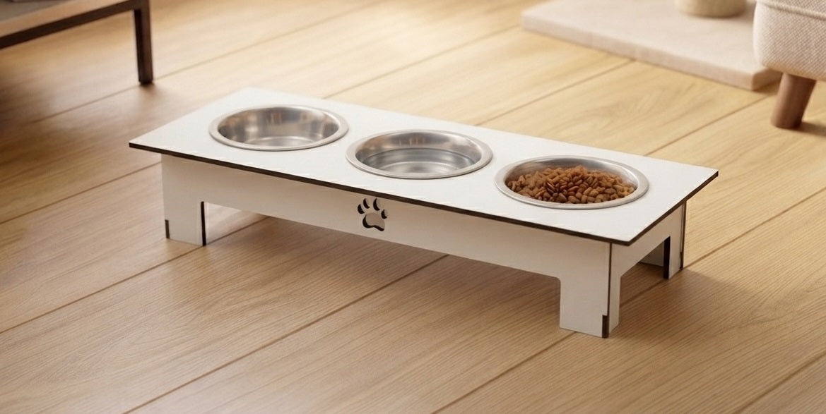 A white elevated pet feeder and water bowl stand with three stainless steel bowls, one filled with dry kibble, placed on a light wood floor.
