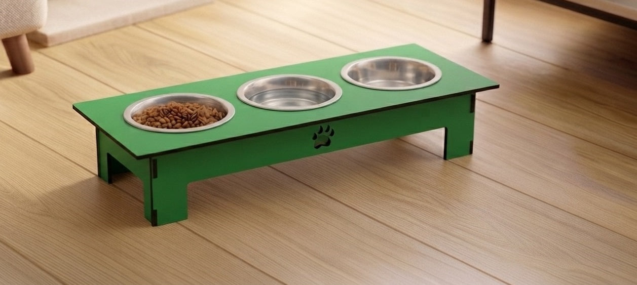 A green elevated pet feeder with three stainless steel bowls, one filled with dry dog food, placed on a light wood floor.
