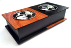 A two-bowl elevated pet feeder and waterer with a black metal body, a reddish-brown wood-grain top panel, and two stainless steel bowls, shown on a white background.