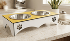 A double pet feeder and waterer stand with a red top surface and stainless steel bowls, featuring a white base with paw print cutouts, shown on a white background.