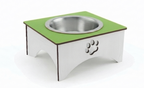 A square elevated pet feeder and water bowl stand with a green top surface, a stainless steel bowl, and a white base featuring a laser-cut paw print.