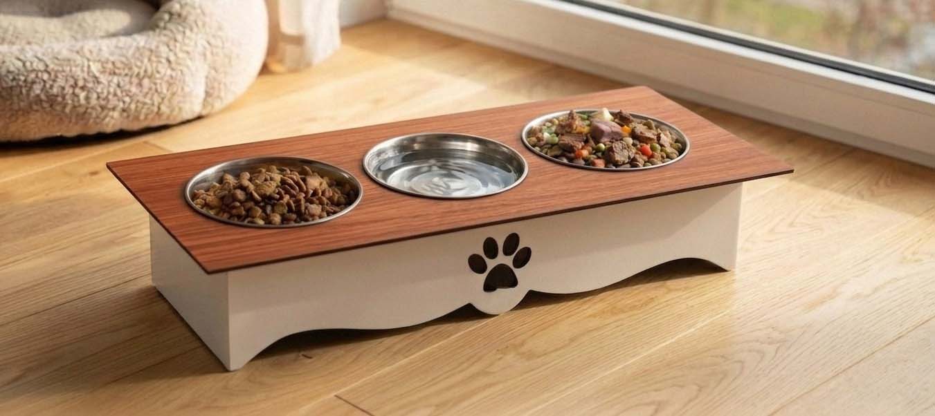 An elevated pet feeder and water bowl stand with a wood-grain top, two metal bowls, and a white base with a black paw print, shown on a wooden floor near a window.