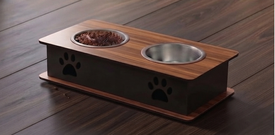 A two-bowl pet feeder and waterer elevated on a wooden platform with black paw-print cutouts, shown on a dark wood floor. One bowl contains dry food.