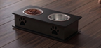 A black elevated double pet feeder with a raised platform, two bowls (one filled with kibble, one empty), and black paw print cutouts on the front, set on a dark wood floor.