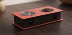 A two-bowl pet feeder and water bowl stand with a matte red top and base, and a black body featuring black paw print cutouts. The stainless steel bowl on the left is empty, while the right bowl contains dry dog food.