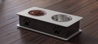 A two-bowl elevated pet feeder and water fountain with a white top tray, dark gray base, and black paw print cutouts, shown on a dark wood floor. One bowl contains wet food.