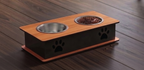 An elevated pet feeder and water bowl stand with a light wood top, black base, and paw print details, shown on a dark wood floor. One bowl is empty and the other contains dog food.