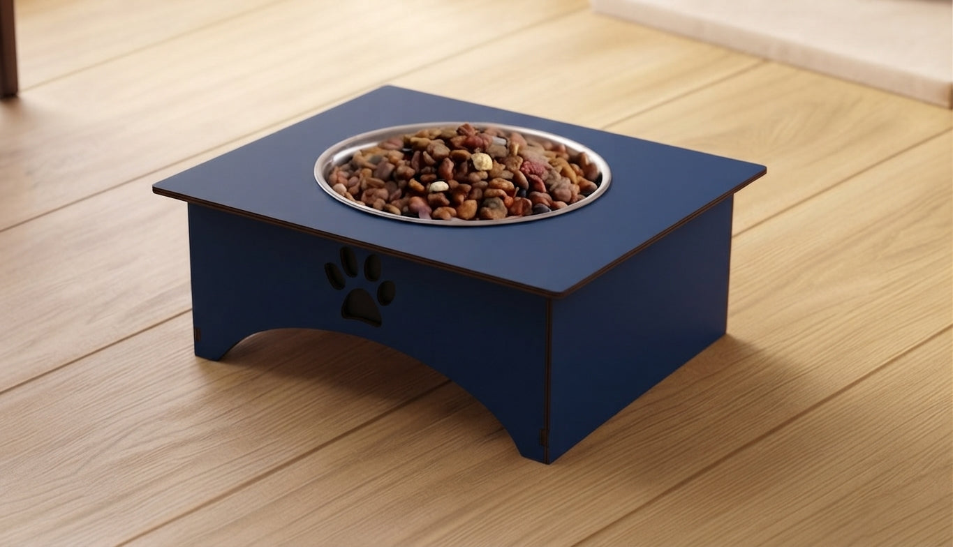 A navy blue elevated dog feeder with a stainless steel bowl filled with kibble, placed on a light wood floor.