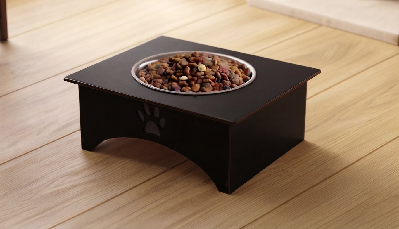 A black elevated pet feeder with a stainless steel bowl filled with dry dog food, placed on a light wood floor.