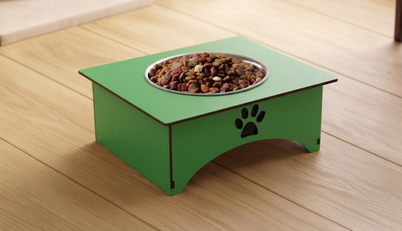 A green elevated pet feeder with a stainless steel bowl filled with kibble, placed on a light wood floor. The feeder has a black paw print design on the front side.