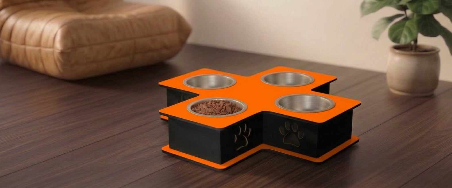 A four-bowl elevated pet feeder and waterer with a bright orange top and black base, placed on a dark wooden table in a home setting with a cushion and potted plant in the background.