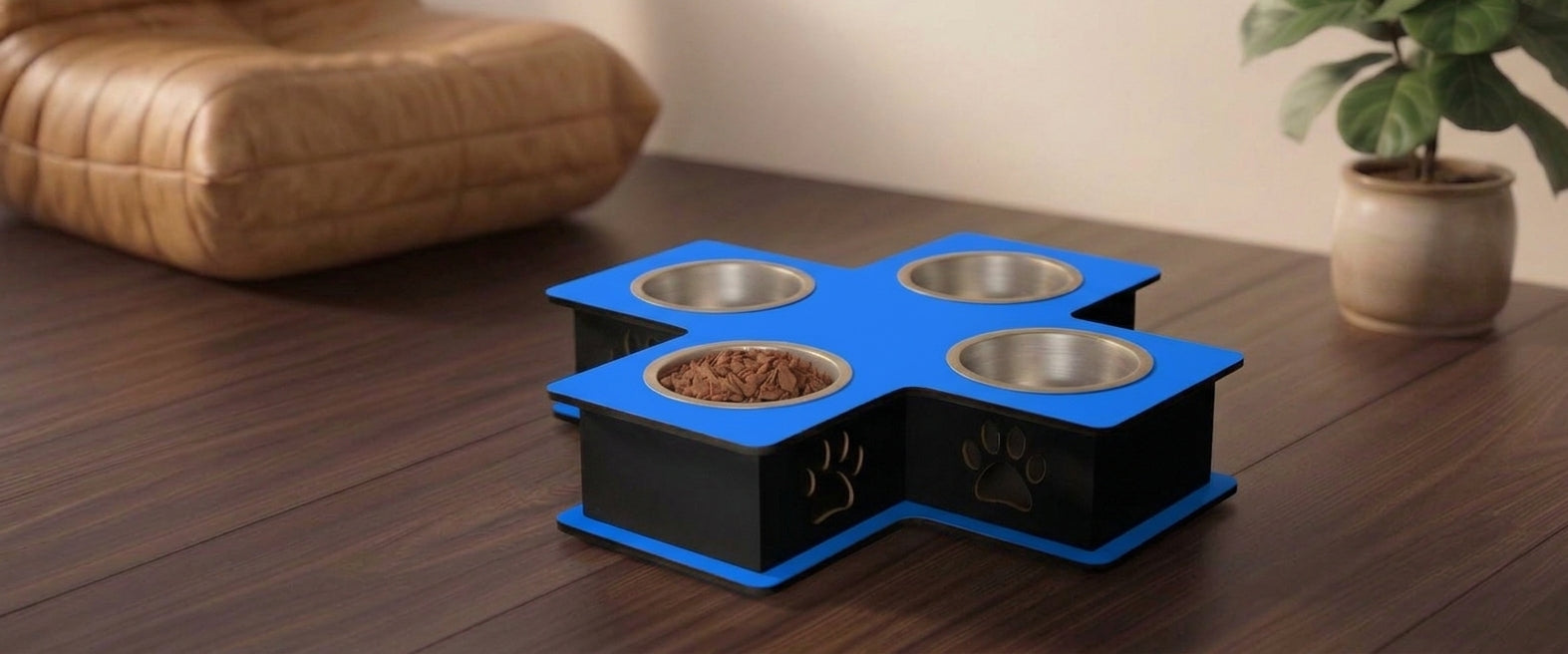A four-bowl elevated pet feeder and waterer with a blue top and black base, shown on a dark wooden table in a home setting with a cushion and potted plant in the background.