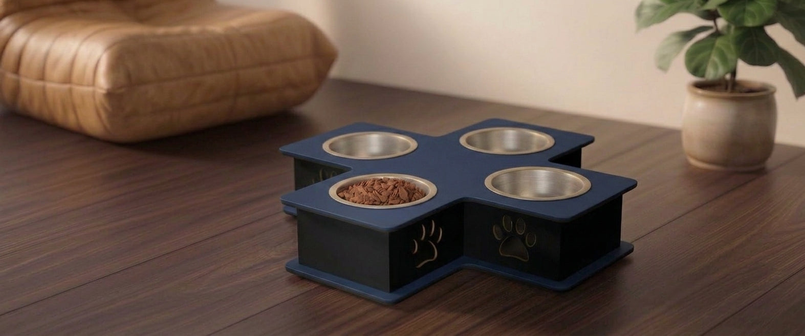 A four-bowl elevated pet feeder and waterer with a dark blue cross-shaped base, stainless steel bowls, and gold paw print details, shown on a wooden table in a home setting.