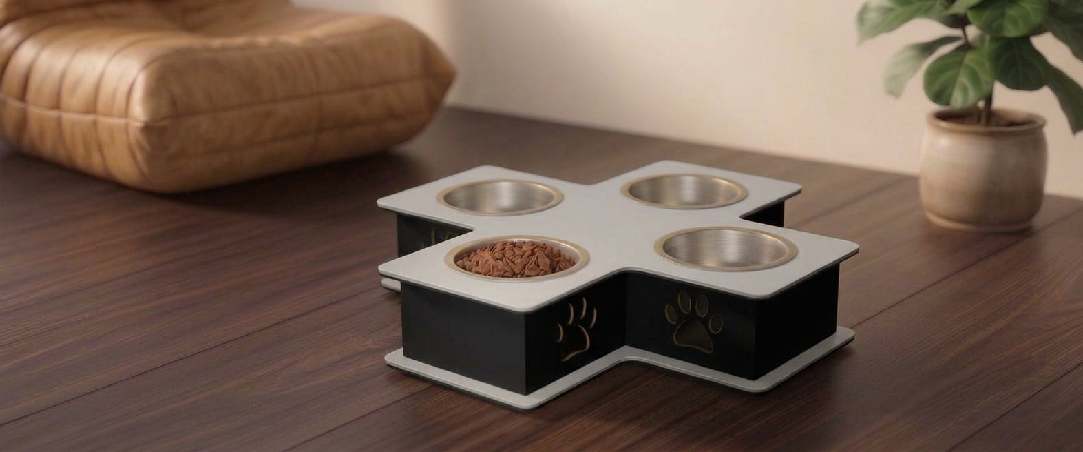A four-bowl elevated pet feeder and waterer with a black and white cross-shaped base, shown on a dark wooden table in a home setting with a cushion and a potted plant in the background.