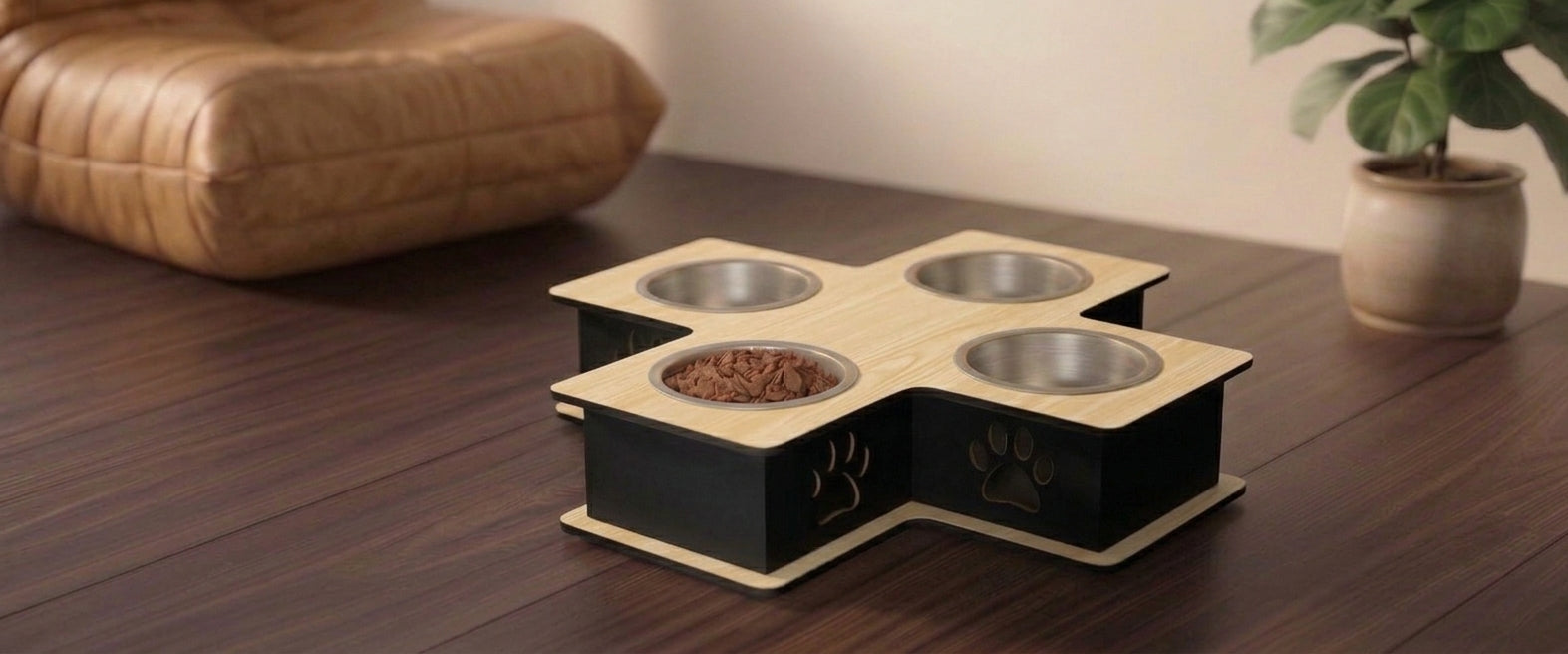 A four-bowl elevated pet feeder and waterer with a light wood top and black base, shown on a dark wooden table in a home setting with a cushion and potted plant in the background.