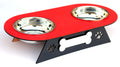 A two-bowl pet feeder and waterer stand with a red top tray, stainless steel bowls, and a black triangular base decorated with a bone and paw print cutout.