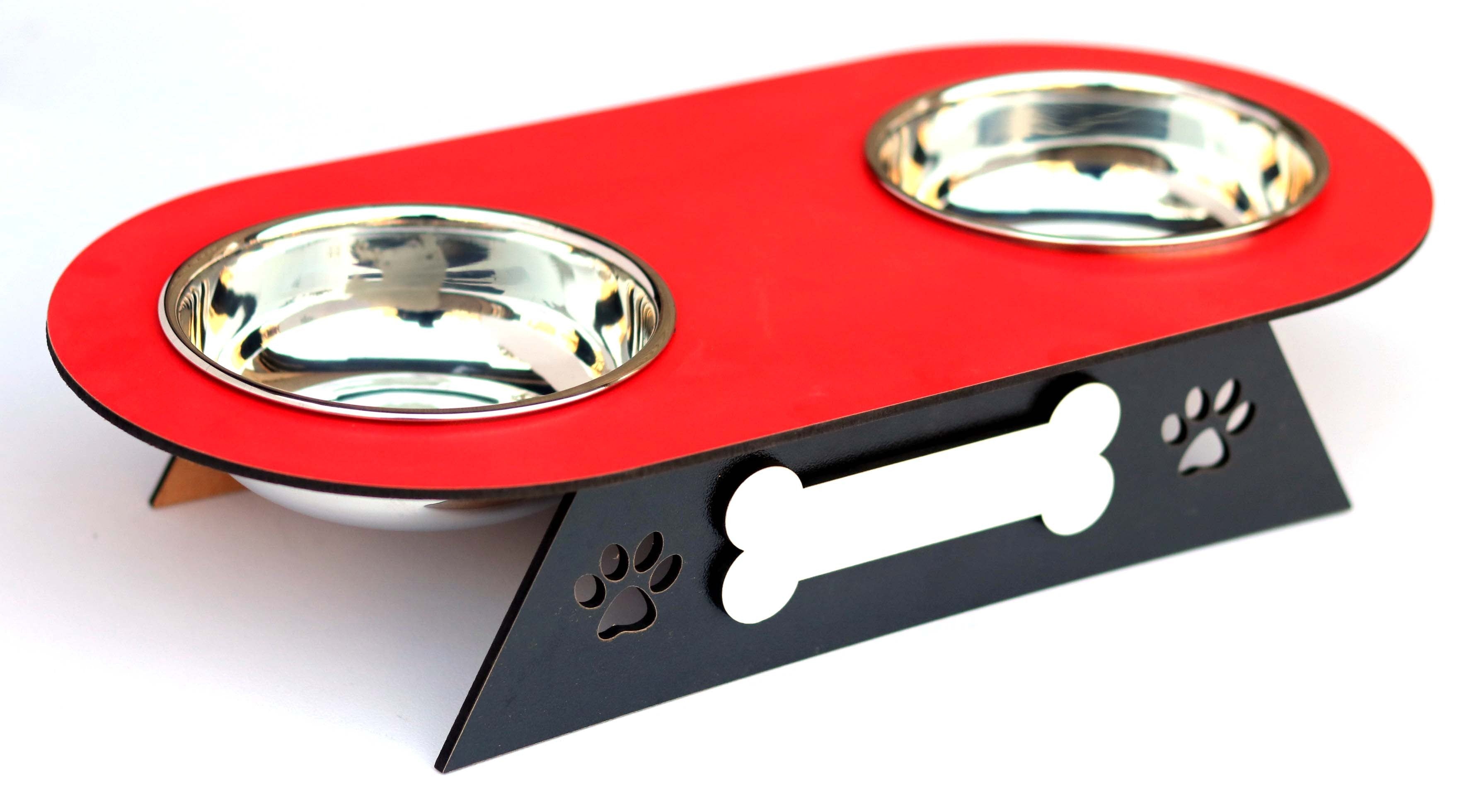 A two-bowl pet feeder and waterer stand with a red top tray, stainless steel bowls, and a black triangular base decorated with a bone and paw print cutout.