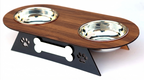 A two-bowl pet feeder and waterer stand with a dark brown wood-grain top, two stainless steel bowls, and a black metal base with bone and paw print cutouts, shown on a white background.