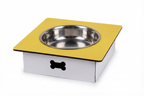 A square pet feeder or elevated bowl stand with a yellow top platform, a stainless steel bowl, and a white base featuring a black bone-shaped cutout, shown on a white background.