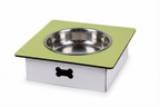 A square elevated pet feeder and water bowl stand with a light green top surface, a stainless steel bowl, and a white base with a black bone-shaped cutout, shown on a white background.