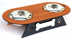 A two-bowl pet feeder and waterer stand with a brown wood-grain top, stainless steel bowls, and a black metal base with bone and paw print cutouts, shown on a white background.