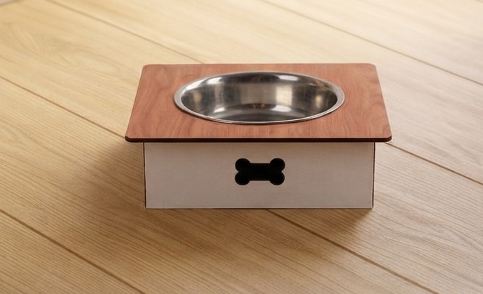 A pet elevated feeder with a square wooden top, a stainless steel bowl, and a white base with a black bone-shaped cutout, shown on a light wood plank floor.