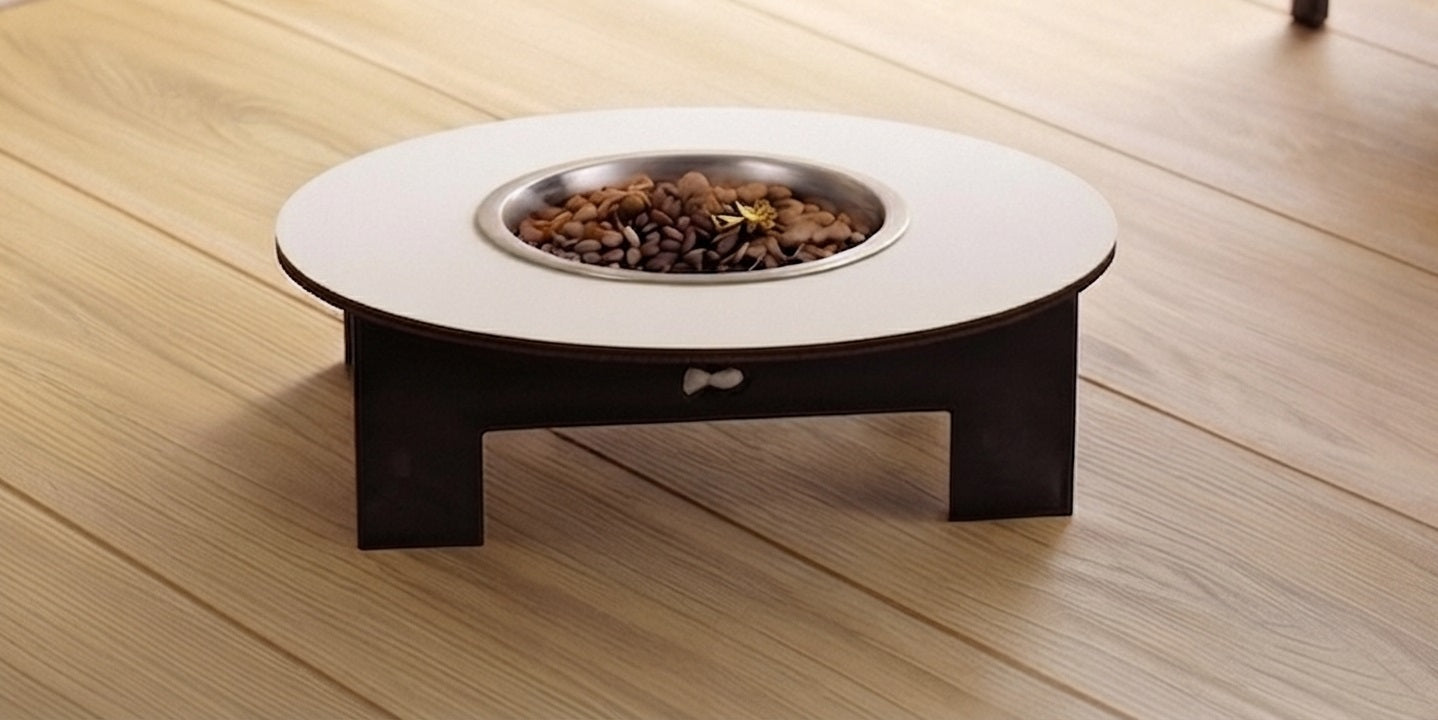 A low-profile elevated pet feeder table with a round white top, dark brown wooden legs, and a stainless steel bowl filled with kibble, set on a light wood plank floor.