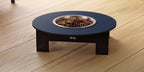 A round elevated pet feeder table with a dark blue top, black legs, and a stainless steel bowl filled with kibble, set on a light wood plank floor.