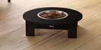 A low-profile black pet fire pit table with a circular stainless steel bowl filled with dark coffee beans, set on a light wood plank floor.