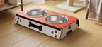 A pet elevated double bowl feeder with stainless steel bowls, set on a light wood floor in a home environment.