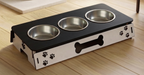 A three-bowl elevated pet feeder and waterer stand with a black top tray and white side panels decorated with paw prints and a bone cutout, shown on a light wood floor.