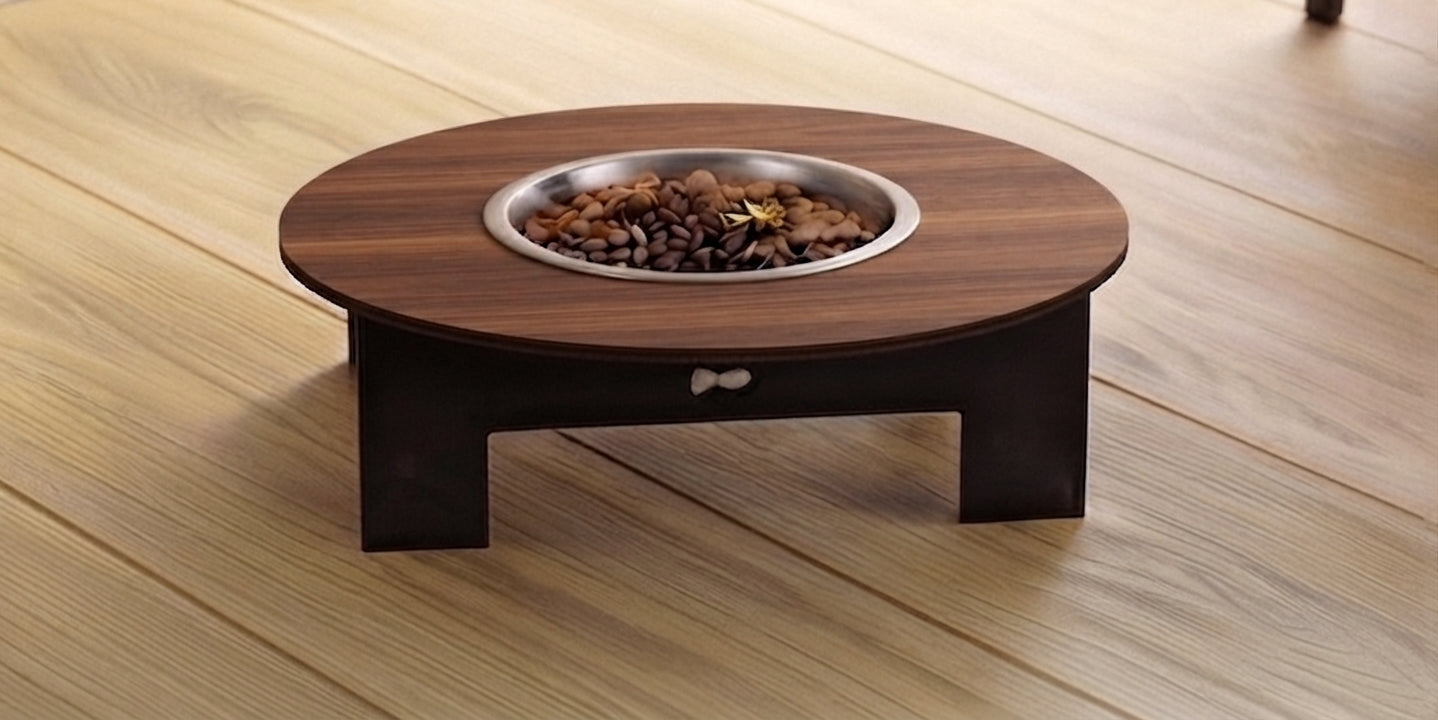A round wooden pet fire table with a dark brown wood-grain top, a small drawer, and a stainless steel fire bowl filled with rocks, set on a light wood plank floor.